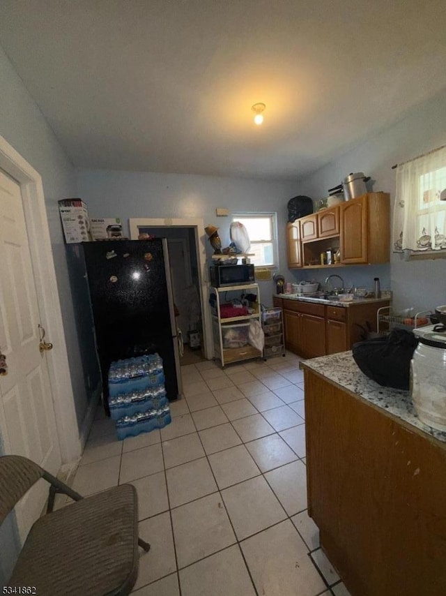 kitchen featuring brown cabinetry, black microwave, open shelves, a sink, and light tile patterned flooring