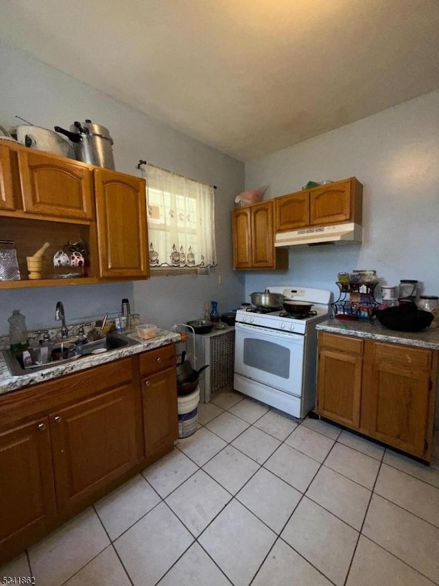 kitchen with gas range gas stove, light tile patterned floors, brown cabinetry, a sink, and under cabinet range hood