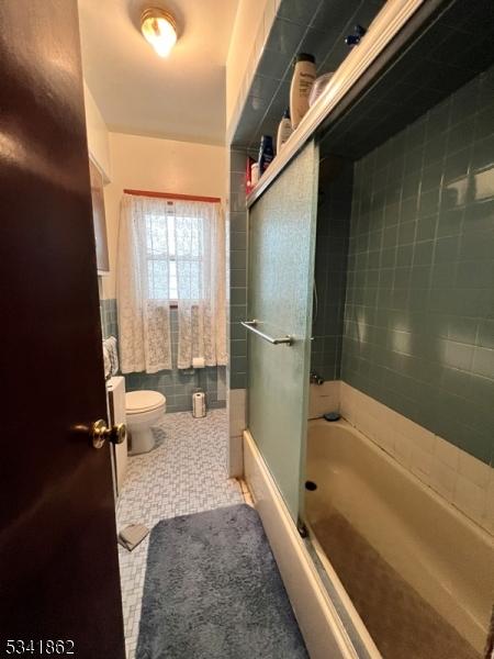 full bathroom featuring shower / bath combination with glass door, toilet, and tile patterned floors