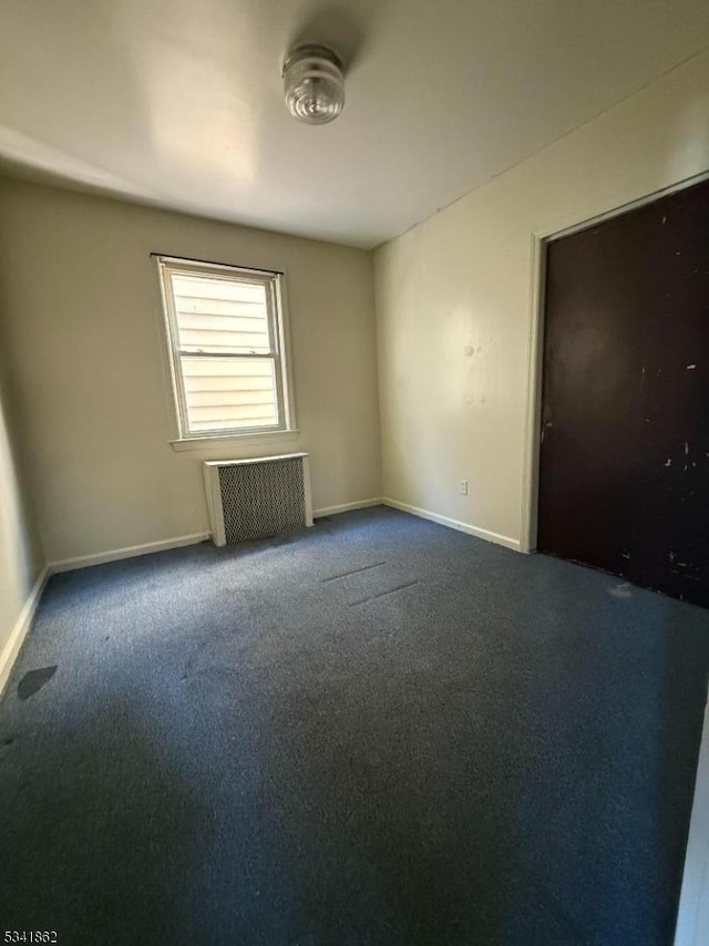 spare room with radiator heating unit, dark carpet, and baseboards