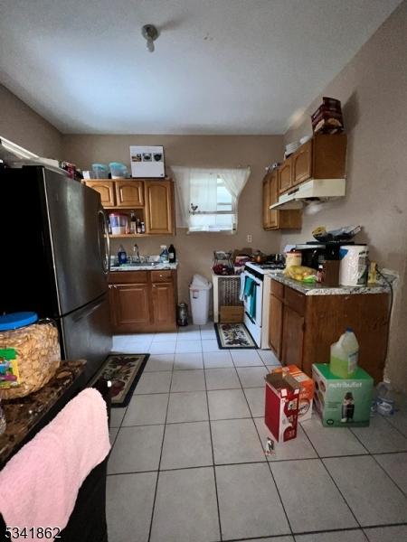 kitchen featuring brown cabinets, light tile patterned floors, freestanding refrigerator, white range with gas cooktop, and under cabinet range hood