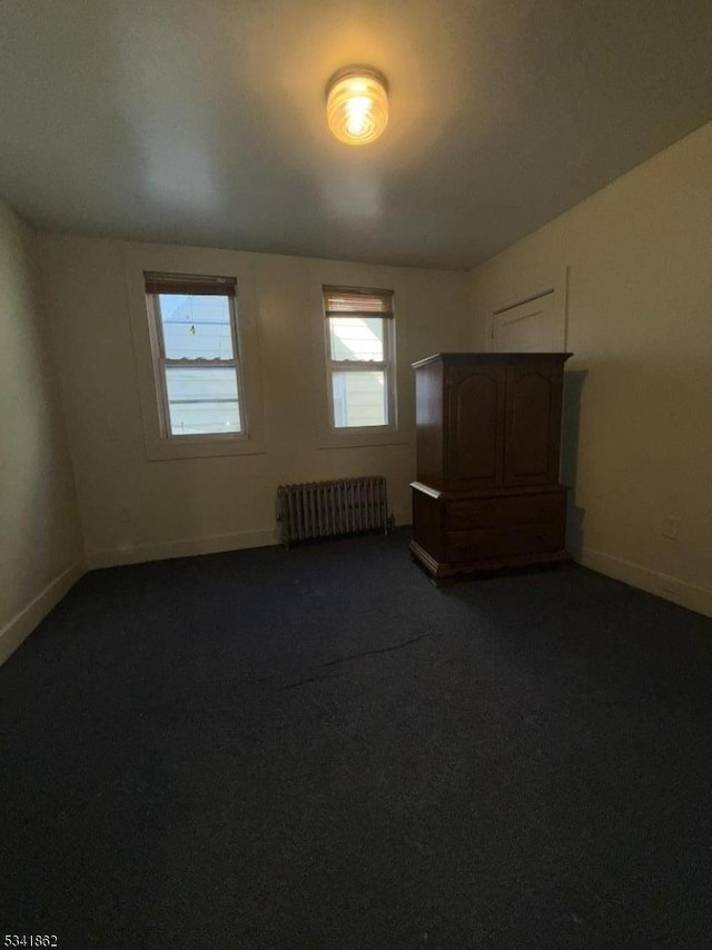 unfurnished room featuring radiator heating unit, baseboards, and dark colored carpet