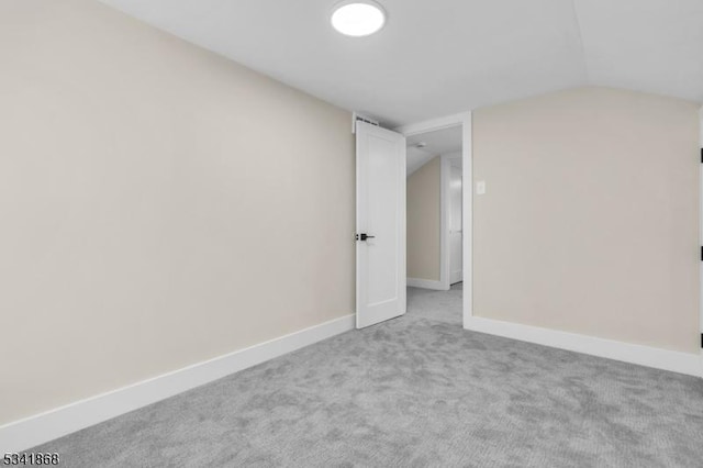 carpeted empty room featuring lofted ceiling and baseboards