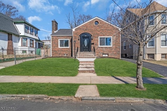 bungalow with brick siding, fence, driveway, a chimney, and a front yard