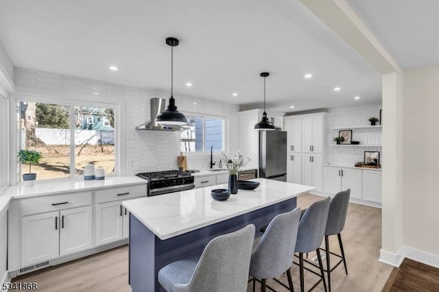 kitchen with wall chimney range hood, gas stove, freestanding refrigerator, and a kitchen breakfast bar