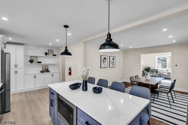 kitchen featuring recessed lighting, white cabinetry, light wood-type flooring, freestanding refrigerator, and stainless steel microwave