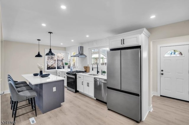 kitchen featuring a sink, appliances with stainless steel finishes, wall chimney range hood, and white cabinetry