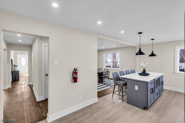 kitchen with light wood finished floors, baseboards, a kitchen island, a kitchen breakfast bar, and light countertops