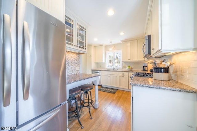 kitchen with appliances with stainless steel finishes, light wood-type flooring, light stone countertops, and tasteful backsplash