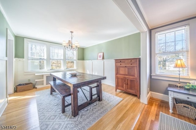 dining room with ornamental molding, wainscoting, light wood-style flooring, and an inviting chandelier