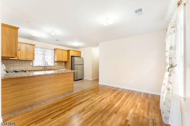 kitchen featuring visible vents, decorative backsplash, stainless steel appliances, light wood-type flooring, and a sink