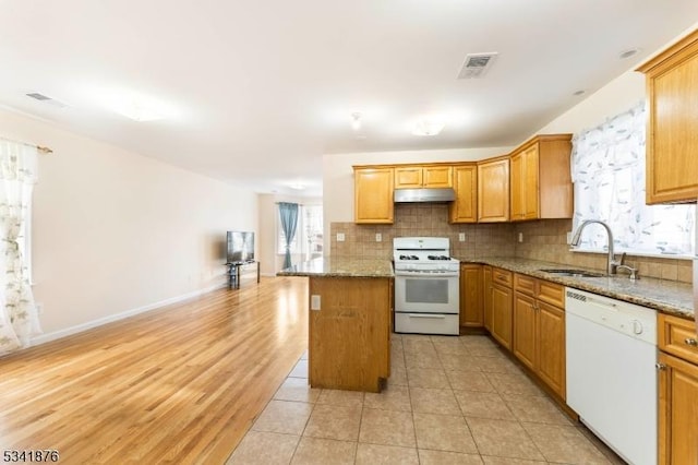 kitchen featuring white appliances, stone countertops, a sink, under cabinet range hood, and backsplash