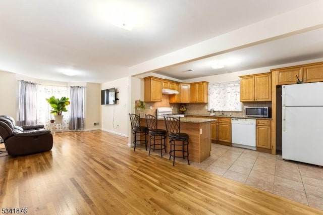 kitchen with decorative backsplash, open floor plan, white appliances, plenty of natural light, and a kitchen bar