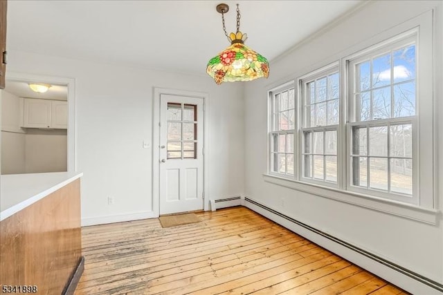 unfurnished dining area featuring a baseboard heating unit, light wood-type flooring, and baseboards