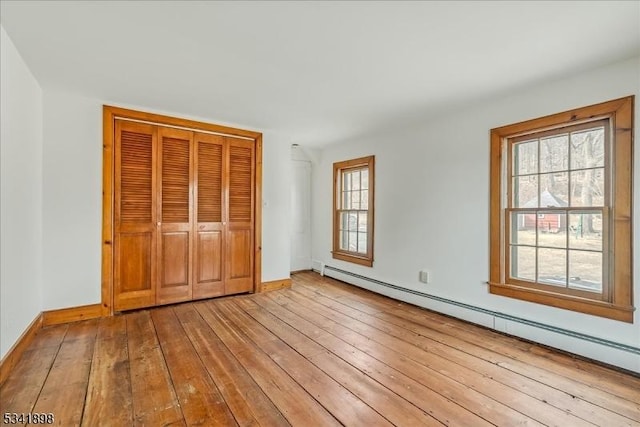 unfurnished bedroom featuring a closet, baseboards, baseboard heating, and hardwood / wood-style flooring