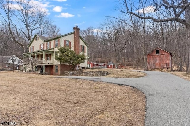 view of home's exterior with an outbuilding, a chimney, a barn, driveway, and stairs