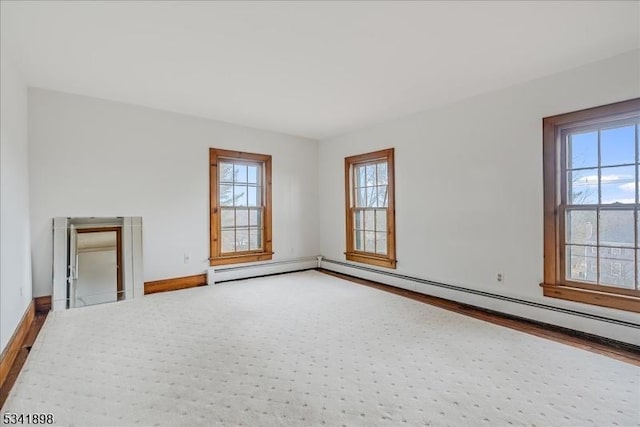 unfurnished room with a baseboard heating unit, baseboards, and wood finished floors