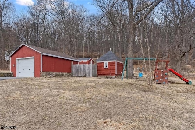 view of yard with an outbuilding, a playground, fence, and a detached garage