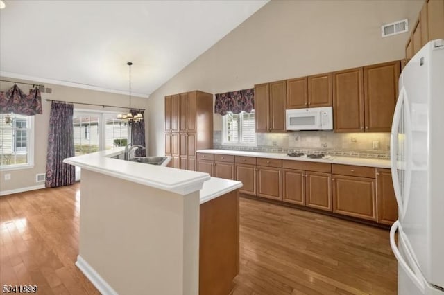 kitchen featuring white appliances, visible vents, light wood finished floors, a sink, and brown cabinets