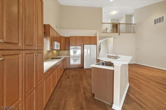 kitchen featuring white appliances, wood finished floors, visible vents, a high ceiling, and a sink