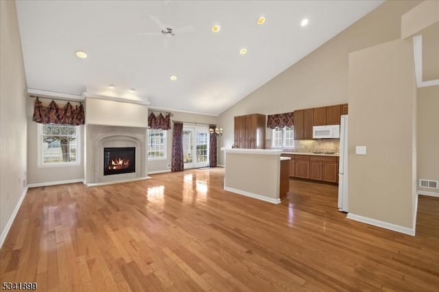 unfurnished living room featuring a glass covered fireplace, baseboards, light wood-type flooring, and high vaulted ceiling