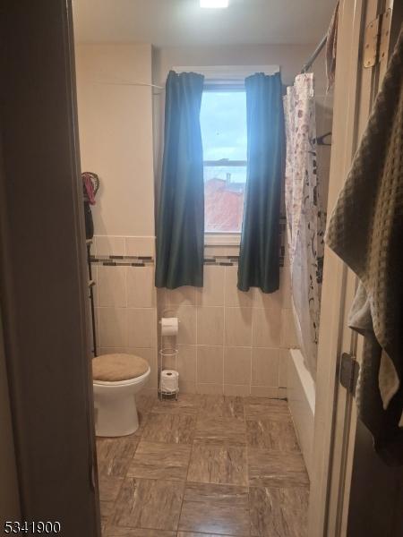 full bath featuring tile walls and toilet