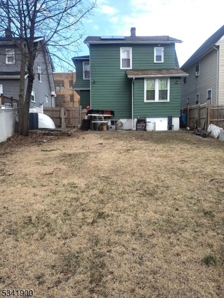 back of property with solar panels, a lawn, a chimney, and fence