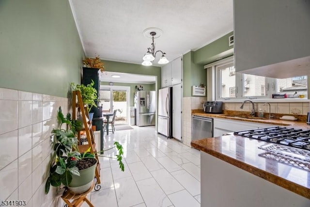 kitchen featuring tile walls, decorative light fixtures, a notable chandelier, stainless steel appliances, and a sink