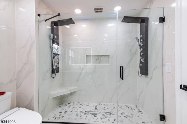 bathroom with toilet, a marble finish shower, visible vents, and tile walls