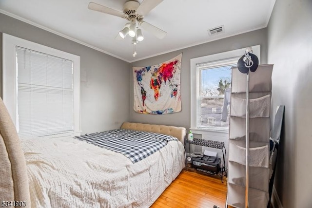 bedroom featuring ornamental molding, a ceiling fan, visible vents, and wood finished floors