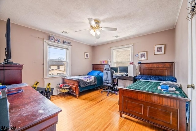 bedroom featuring light wood-style floors, ceiling fan, visible vents, and a textured ceiling