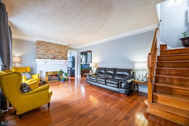 living room featuring wood-type flooring, ornamental molding, a brick fireplace, a textured ceiling, and stairs