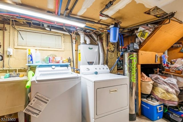 washroom with laundry area, water heater, a sink, and washer and clothes dryer