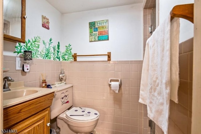 bathroom with toilet, a wainscoted wall, tile walls, and vanity