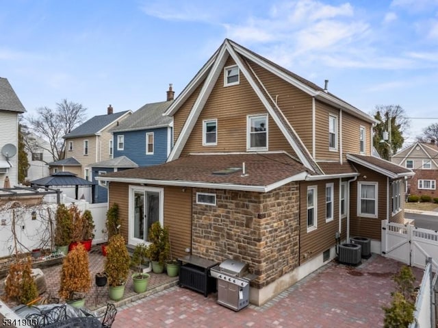 rear view of house featuring central AC unit, a gate, a patio area, fence, and stone siding