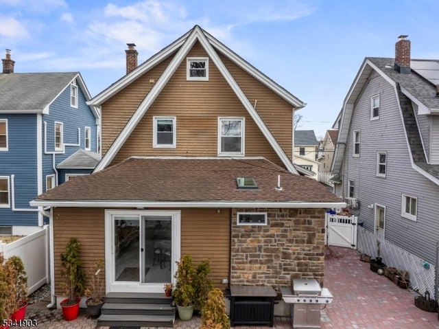 rear view of house featuring entry steps, a shingled roof, fence, a gate, and a patio area