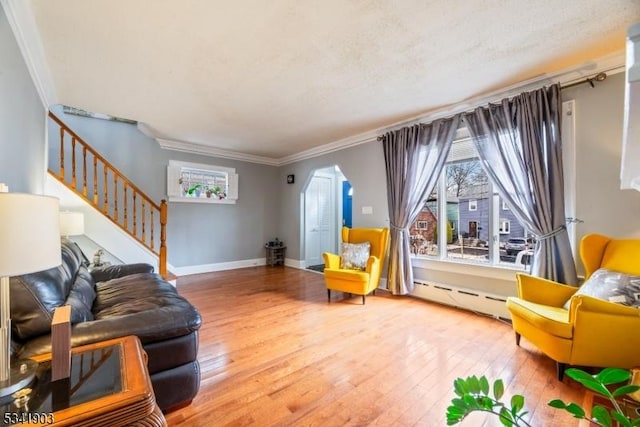 living room featuring wood-type flooring, stairs, baseboard heating, and crown molding