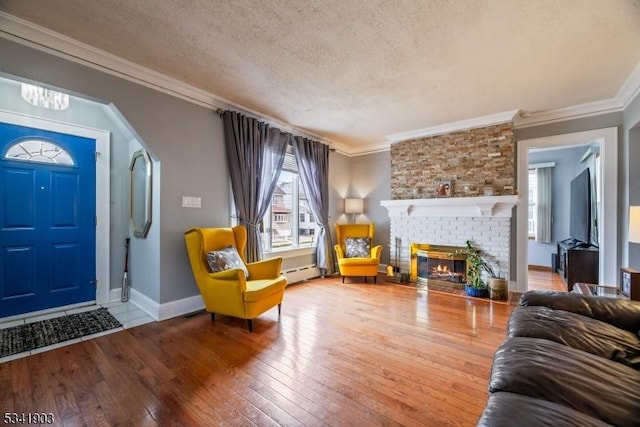 living room featuring a textured ceiling, hardwood / wood-style flooring, a baseboard heating unit, a brick fireplace, and crown molding