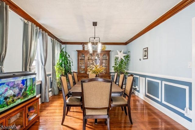 dining room with a chandelier, a decorative wall, a wainscoted wall, wood finished floors, and ornamental molding