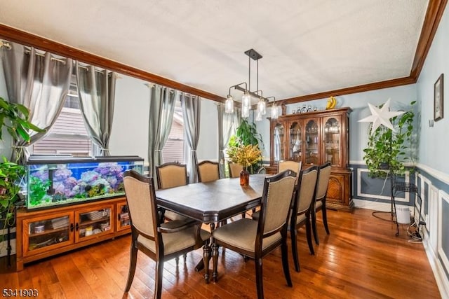 dining area with hardwood / wood-style flooring, ornamental molding, and wainscoting