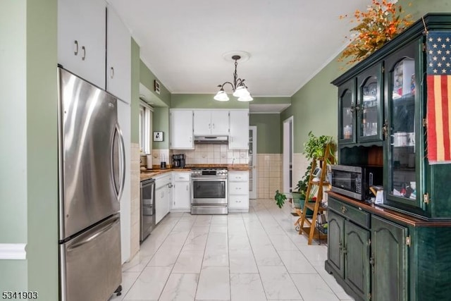 kitchen featuring appliances with stainless steel finishes, white cabinets, ornamental molding, and under cabinet range hood