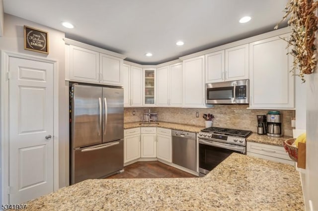 kitchen with stainless steel appliances, glass insert cabinets, backsplash, and light stone countertops