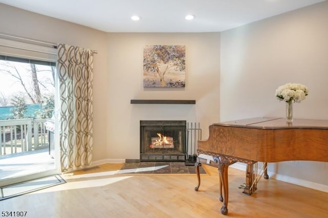 living area featuring a fireplace with flush hearth, baseboards, and wood finished floors