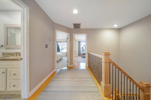 hallway with visible vents, a sink, an upstairs landing, light wood-type flooring, and baseboards