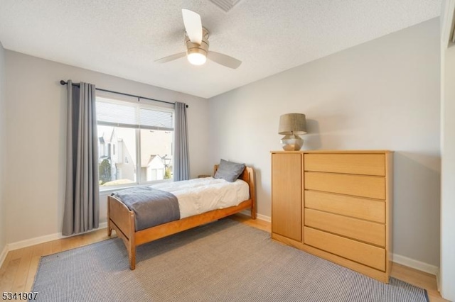 bedroom featuring baseboards, a textured ceiling, and light wood finished floors