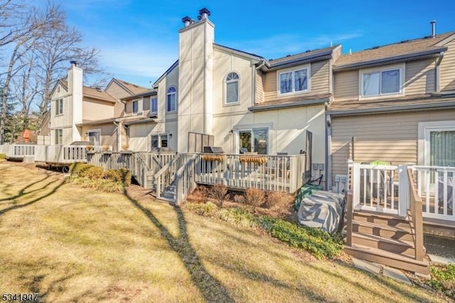 rear view of property featuring a chimney, a yard, a deck, and stucco siding