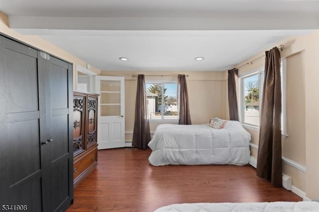 bedroom with a baseboard heating unit, multiple windows, baseboards, and dark wood-style flooring