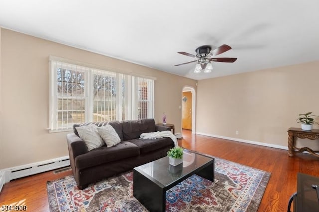 living area with arched walkways, a baseboard heating unit, wood finished floors, and a ceiling fan