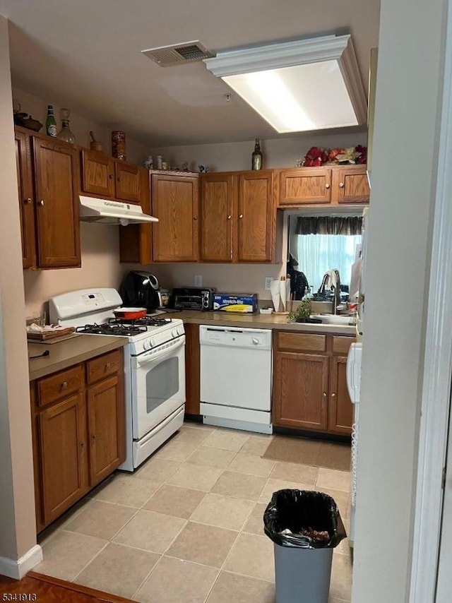 kitchen with visible vents, brown cabinets, a sink, under cabinet range hood, and white appliances