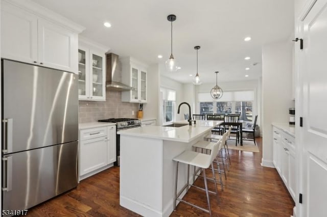 kitchen with a sink, appliances with stainless steel finishes, wall chimney range hood, and white cabinetry